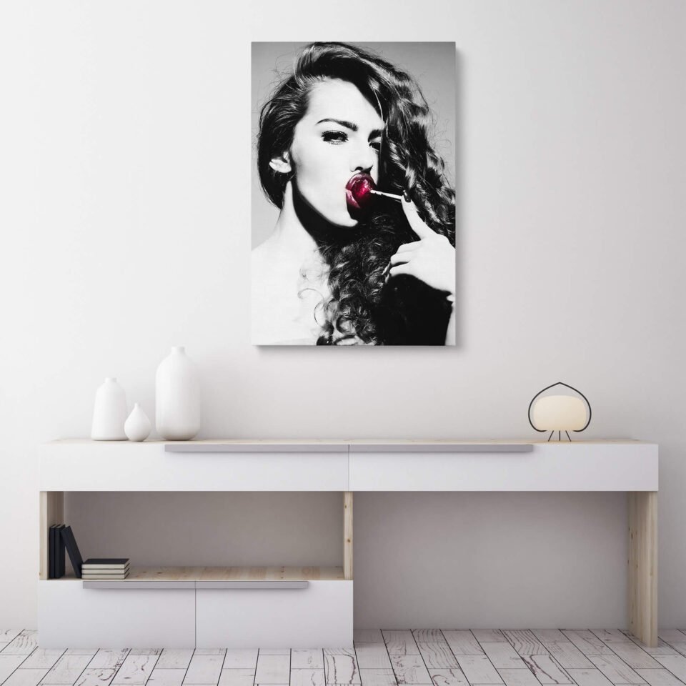Lollipop Seduction - Black and White Portrait with a Woman and a Red Temptation - Canvas Prints. The black-and-white contrast creates a visually captivating effect, highlighting the woman's features and creating a sense of depth and intensity. Her gaze, combined with the placement of the red lollipop on her lips, exudes a playful and seductive energy.